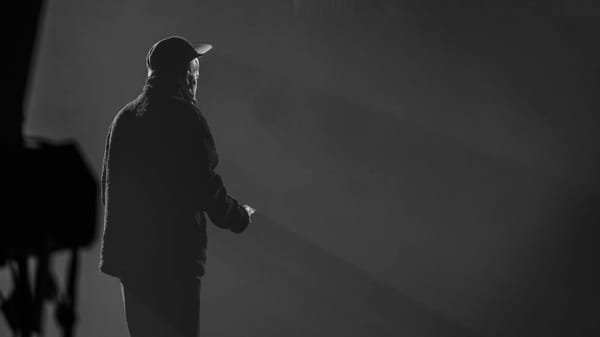 A man stands on a stage, facing an audience, and prepares to give a monologue.